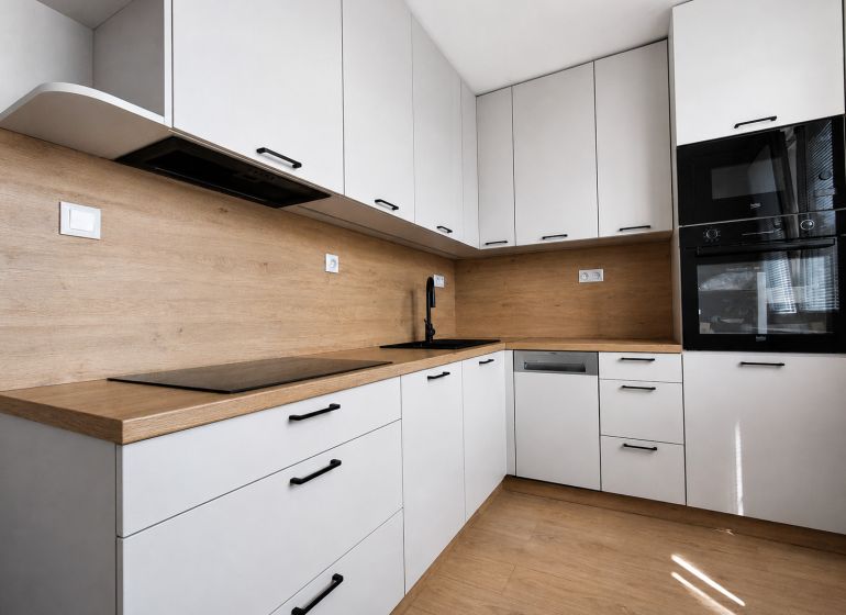 Kompletne zrekonštruovaný 2-izbový byt s 9 m² loggiou Sever - Kuchyňa v 2-izbovom byte s bielymi skrinkami a podlahou s dreveným dekorom.
