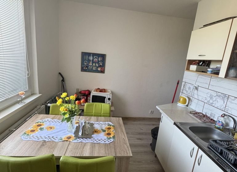 Váš nový štart alebo bezpečná investícia v srdci Šiah - Kuchyňa v 2-izbovom byte s jedálenským stolom, zelenými stoličkami a kvetinovou výzdobou.