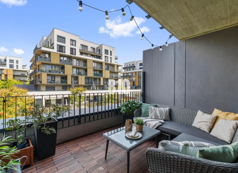 1-IZBOVÝ BYT S VEĽKOU 12 m² TERASOU | SLNEČNICE VILADOMY - Balkón s pohodlným sedením a výhľadom na moderné budovy na Fialovej v Bratislave V.