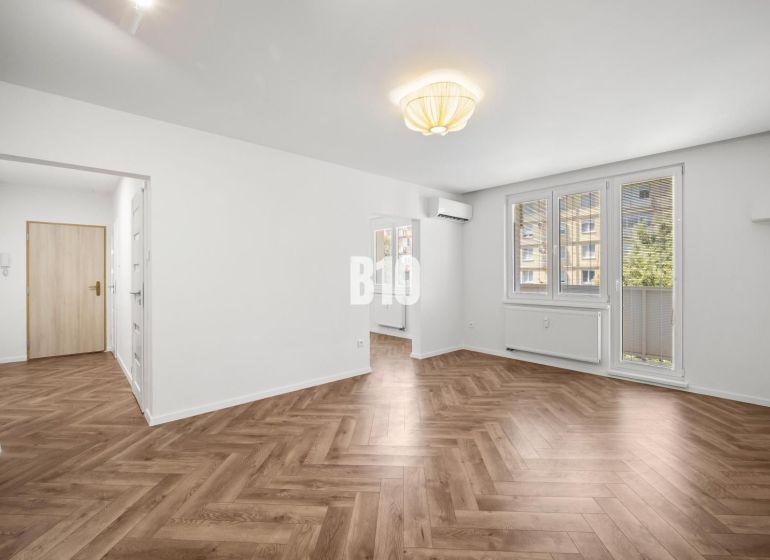 Prémiové bývanie v centre Nitry | 3 izby, veľký balkón - Obývacia izba v 3-izbovom byte so vzorovanou podlahou s dreveným dekorom.