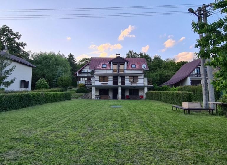 Trojpodlažná rekreačná chata  stredisko Kamenec - Zemplínska Šírava - Chata v Kaluži obklopená zeleňou, udržiavaný trávnik, okolie s drevinami, modrá obloha.