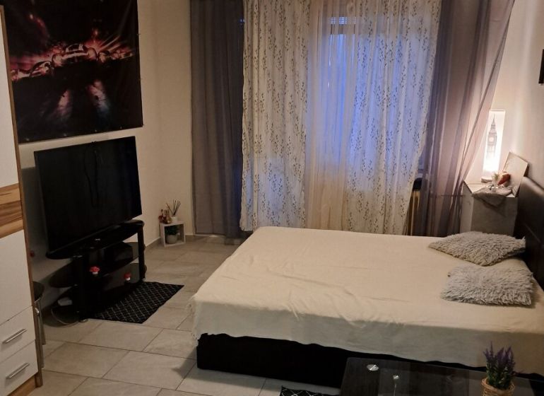 Garzónka, Rybničná ul., BA III - Vajnory - Garsónka so sivo-bielymi stenami, posteľou, televízorom a dlažbou na podlahe.