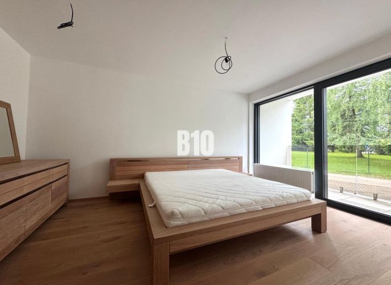 Relax Residence - Apartmán so zariadením - Spálňa s posteľou a komodou, podlaha s dreveným dekorom, veľké okno smerujúce do záhrady.
