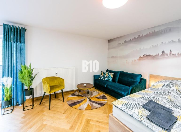 Investičný APARTMÁN v centre Terchovej - Štýlový rekreačný apartmán s podlahou s dreveným dekorom, pohovkou a rastlinami.