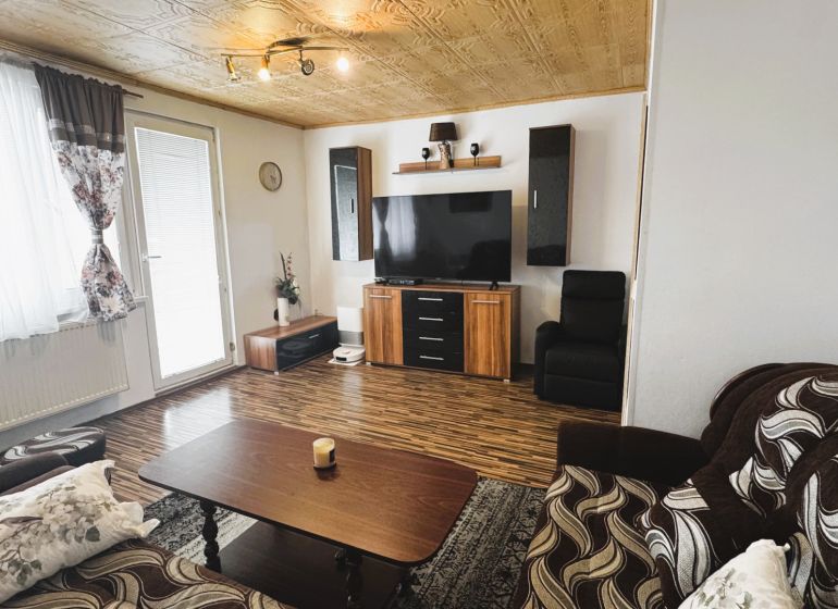 94,66 m², štyri izby a nikto nad hlavou. A Komenského má svoje výhody! - Obývacia izba v 4-izbovom byte s podlahou s dreveným dekorom a televízorom na stene.