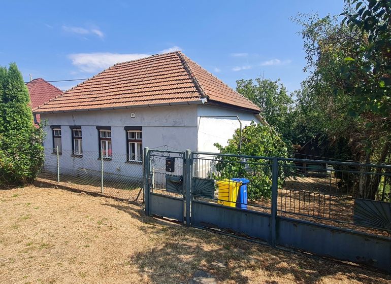 RD Otrokovce 1071m pozemok - Rodinný dom v Dolných Otrokovciach s plotom a záhradou na slnečnom pozemku.