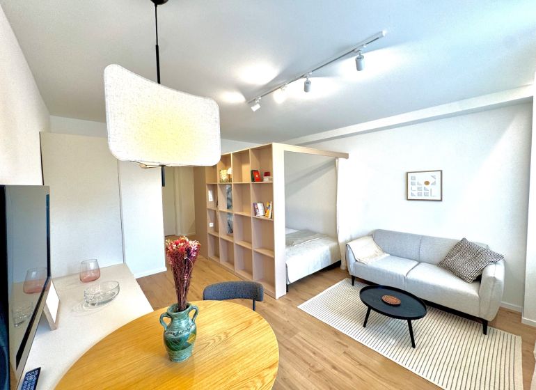 Na predaj úplne nový 1i byt od architekta v tichej časti Dúbravky - Obývacia izba s podlahou s dreveným dekorom, svetlou pohovkou a jedálenským stolom v 1-izbovom byte.
