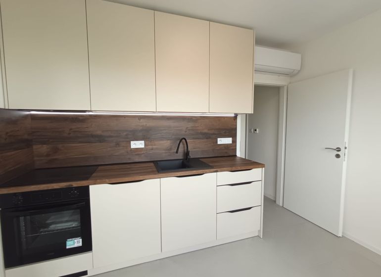 ? Na prenájom: moderný 2 izbový byt – Residence Majakovského, Lučenec - Kuchyňa v 2-izbovom byte s bielymi skrinkami a podlahou s dreveným dekorom.