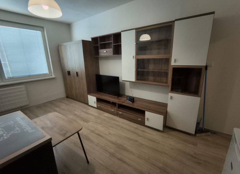 KOMPLET ZARIADENÁ GARSÓNKA PRI PLAVÁRNI - Garsónka s podlahou s dreveným dekorom, skrinkami a televízorom.