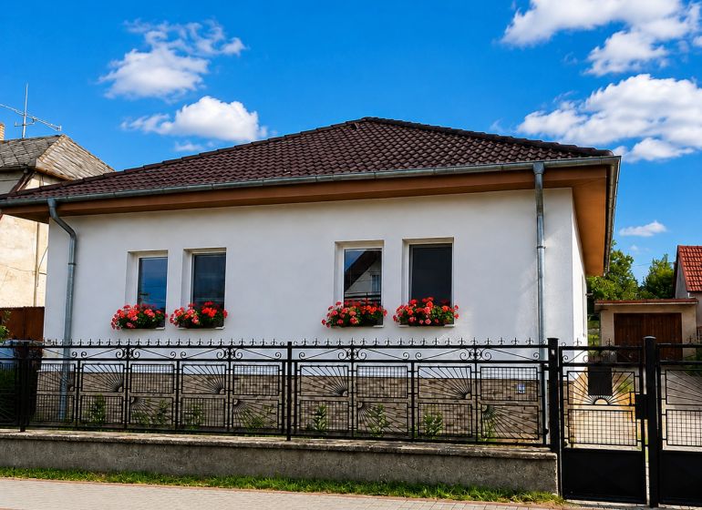 Na predaj zrekonštruovaný 4-izbový rodinný dom v Šalgočke  - Rodinný dom v Šalgočke s bielou fasádou, okennými kvetmi a valbovou strechou.