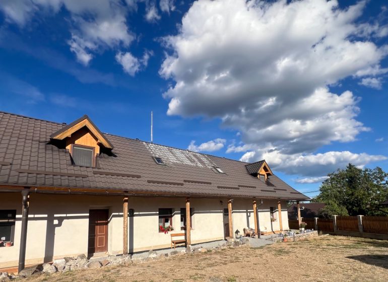 Atraktívny rodinný dom s veľkým pozemkom  – Hronská Dúbrava - Rodinný dom v Hronskej Dúbrave s veľkou strechou a skalnatým chodníkom v záhrade.