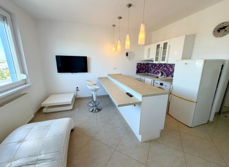 Na predaj kompletne prerobený 1 izbový byt, Vráble - Lúky, 36m2, 7/7 - Kuchyňa v 1-izbovom byte s barovými stoličkami a fialovým obkladom na stene.