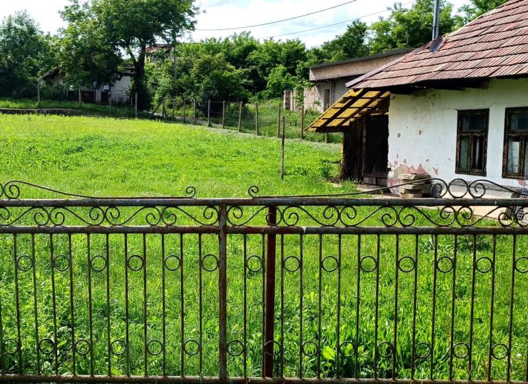 NA PREDAJ stavebný pozemok  v Plavých Vozokanoch - Starší dom s plotom na pozemku, obklopený zeleňou, ideálny pre bývanie.