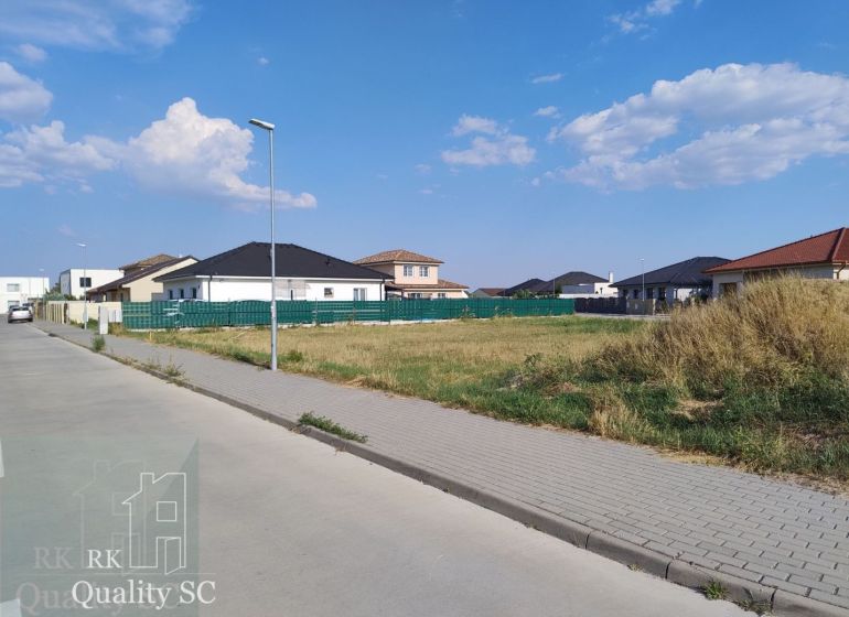 SENEC - NA PREDAJ exkluzívny stavebný pozemok pre rodinné domy - JUŽNÁ - Pozemky na bývanie v Senci obklopené domami a zeleňou pod modrou oblohou.