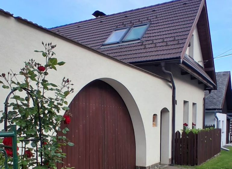 Na predaj rodinný dom, Blatnica - Rodinný dom v Blatnici s tehlovou strechou a kvetmi pozdĺž plotu.