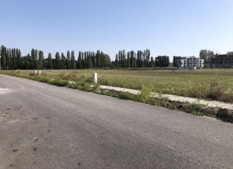 Exkluzívny stavebný pozemok 579 m² – Dunajská Streda, Florida Park - Cesta pri pozemkoch na bývanie v Dunajskej Strede, obklopená zeleňou a budovami.