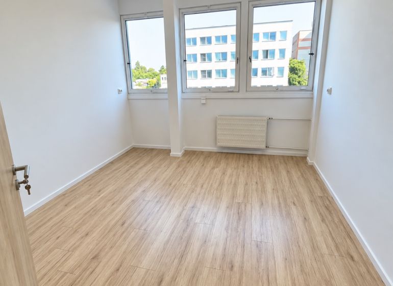 PRENÁJOM KANCELÁRIE 13,5 m² – KOMÁRNO, ZÁHRADNÍCKA ULICA - Kancelária s podlahou s dreveným dekorom, interiér s veľkými oknami a stropným osvetlením.