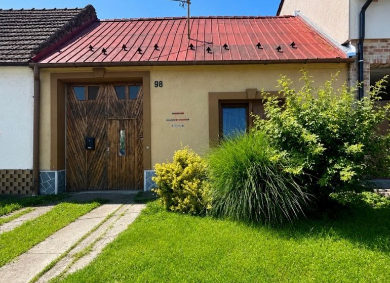 Na predaj starší rodinný dom v obci Budmerice 541m2 - Rodinný dom na Juraja Holčeka v Budmericiach s červenou strechou a zeleným trávnikom.