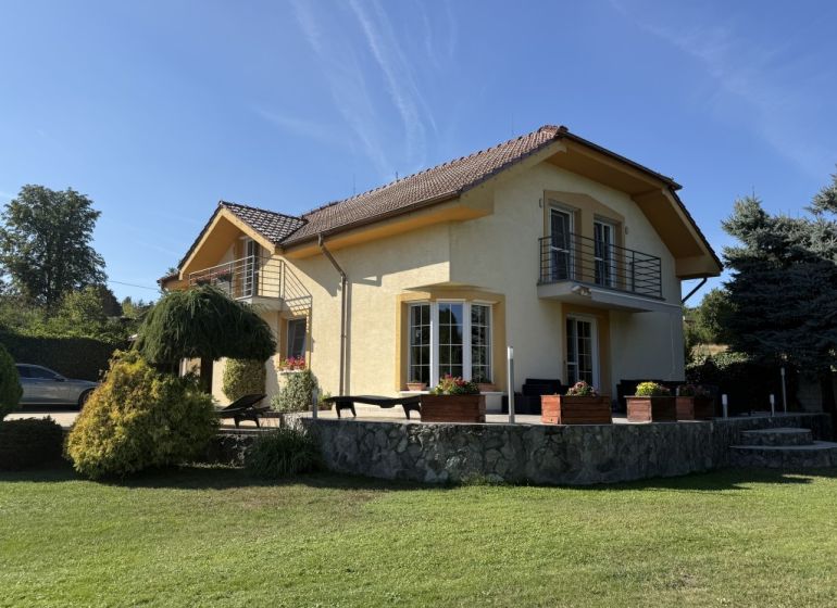 PREDAJ - RODINNÝ DOM - ZLATÉ MORAVCE - Rodinný dom v Zlatých Moravciach, obklopený zeleňou, s kamennou terasou a balkónom.