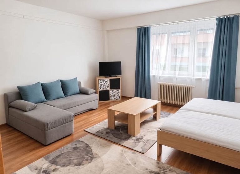Prenájom 1-izbového zariadeného bytu, 43 m² – Šancová - 1-izbový byt s pohovkou, posteľou, televízorom, stolíkom a podlahou s dreveným dekorom.