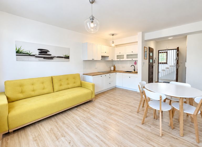 Prenájom 1 izbového bytu v centre obce Oščadnica - Obývačka v 1-izbovom byte s podlahou s dreveným dekorom a žltou sedačkou.