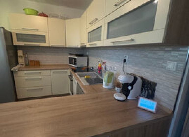 2 iz apartmán v príjemnej lokalite  - Kuchyňa v 2-izbovom byte s podlahou s dreveným dekorom a svetlým nábytkom.