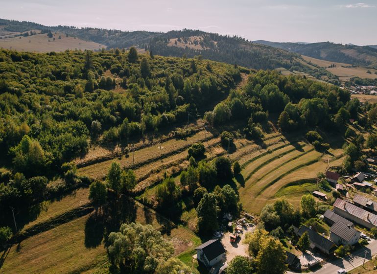 PREDAJ: Pozemky pre rekreačnú chatu, 765 m² – Čierny Balog, Komov - Letecký pohľad na zelené kopce a domy na Školskej ulici v Čiernom Balogu.