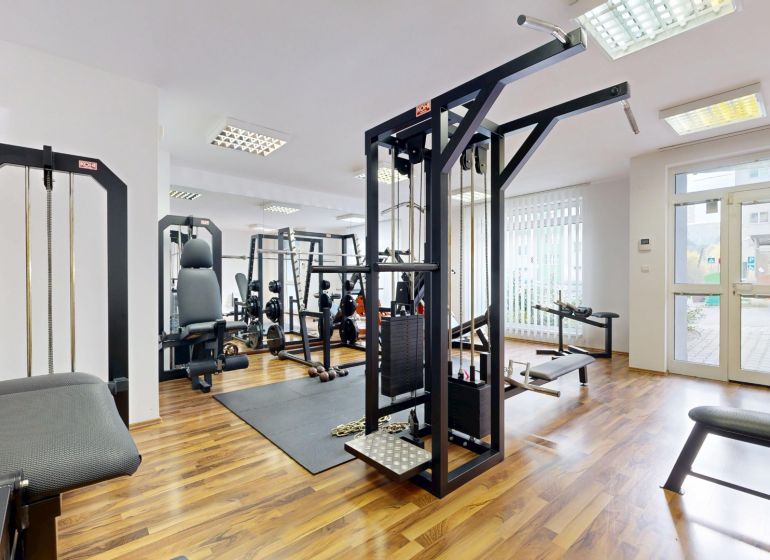 RIVERS | Nebytový priestor v Dúbravke na predaj - Posilňovňa s rôznym fitness vybavením a podlahou s dreveným dekorom v obchodných priestoroch.