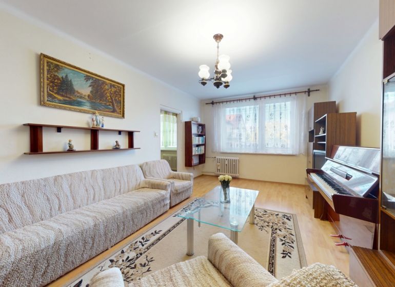 3.izbový byt so záhradou /420 m²/ a chatkou BOŠANY - Obývacia izba v 3-izbovom byte, pohovka, klavír, koberec, podlaha s dreveným dekorom.