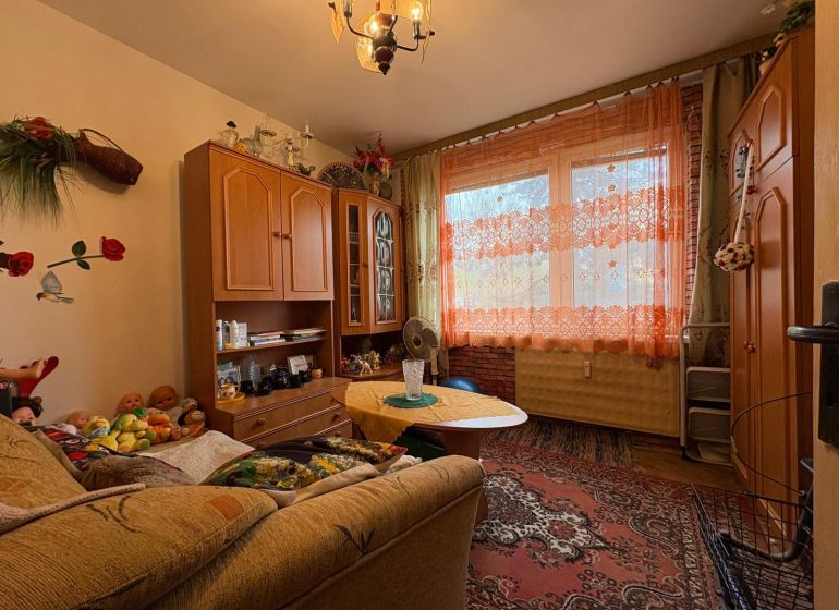 NA PREDAJ 2 izbový byt Nitra - Chrenová - Obývačka v 2-izbovom byte s nábytkom, kobercom a záclonami, podlaha s dreveným dekorom.