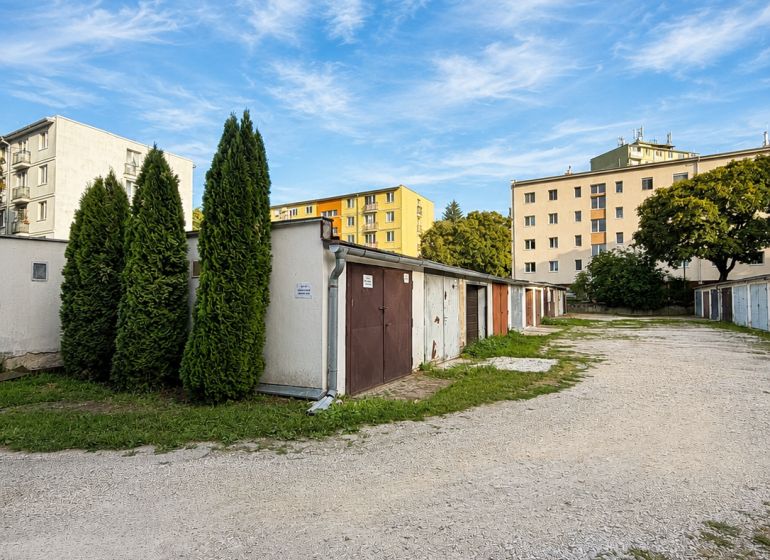PRENÁJOM - Murovaná garáž 18 m² –  Nitra - Garáže na Schurmannovej ulici v Nitre s obytnými domami a modrou oblohou.