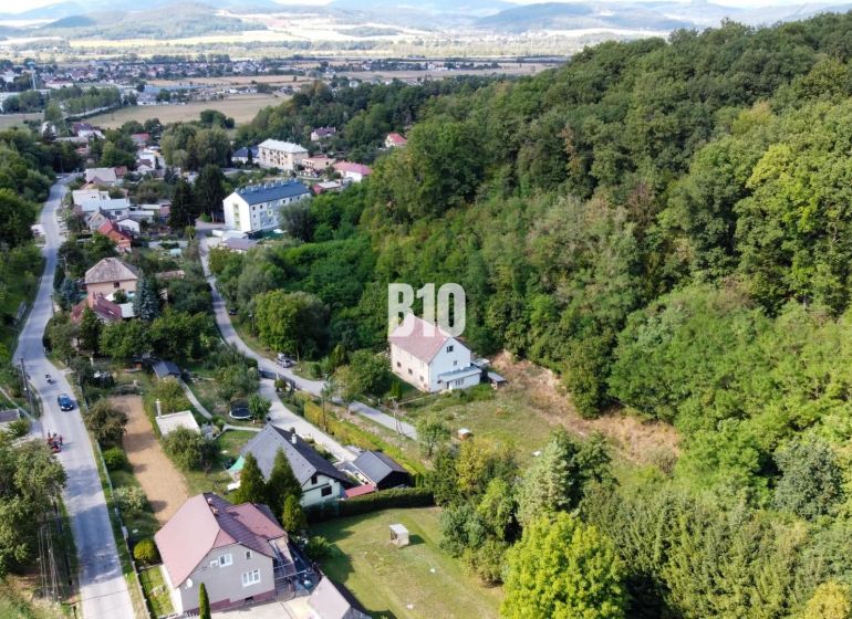 Priestranný 5-izbový rodinný dom na veľkom pozemku pri lese - Letecký pohľad na rodinné domy v obci Ladce, obklopené zelenými svahmi a lesom.