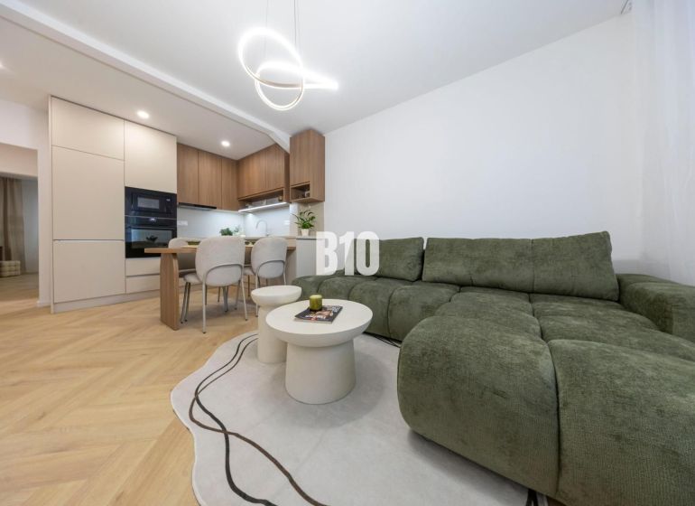 NOVO ZREKONŠTRUOVANÝ 4-IZBOVÝ BYT V TICHOM PROSTREDÍ - 78 m² - NOVÉ ME - Obývacia izba v 4-izbovom byte s podlahou s dreveným dekorom a zelenou sedačkou.
