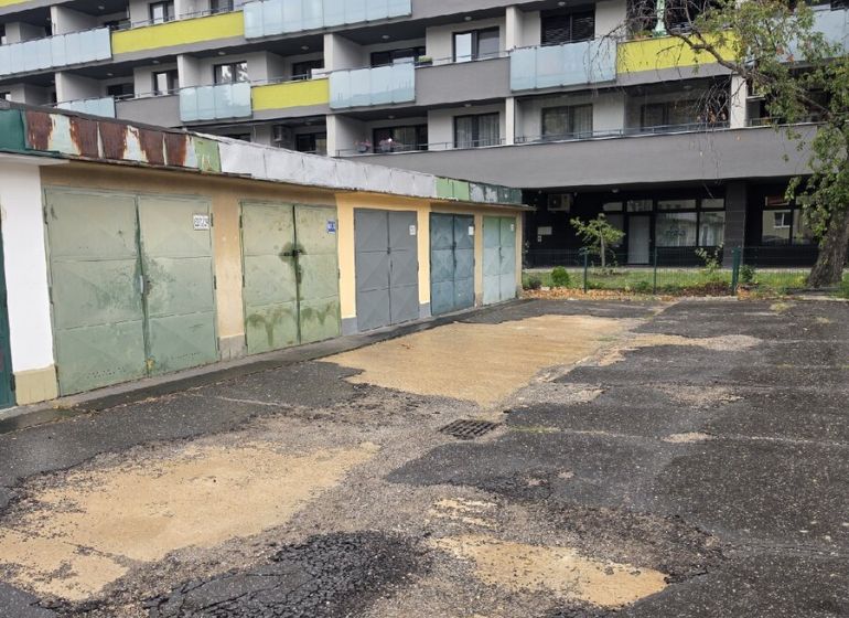 Garáž na Exnárovej ulici  - Garáže na Exnárovej ulici v Bratislave-Ružinove pred bytovým domom s poškodeným asfaltom.
