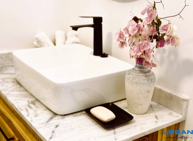 APARTMÁN NA PREDAJ V PAJE, ZANZIBAR - Elegantné umývadlo s keramickou vázou a kvetmi, ideálne pre 1-izbový byt.