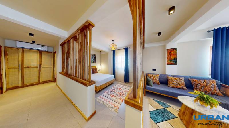 APARTMÁN NA PREDAJ V PAJE, ZANZIBAR - 1-izbový byt s drevenými doplnkami, posteľou, farebným kobercom a pohodlným sedením.