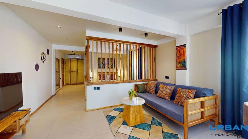 APARTMÁN NA PREDAJ V PAJE, ZANZIBAR - Pohľad na obývačku v a 1-izbovom byte, so stoličkou a drevenými detailami v interiéri.