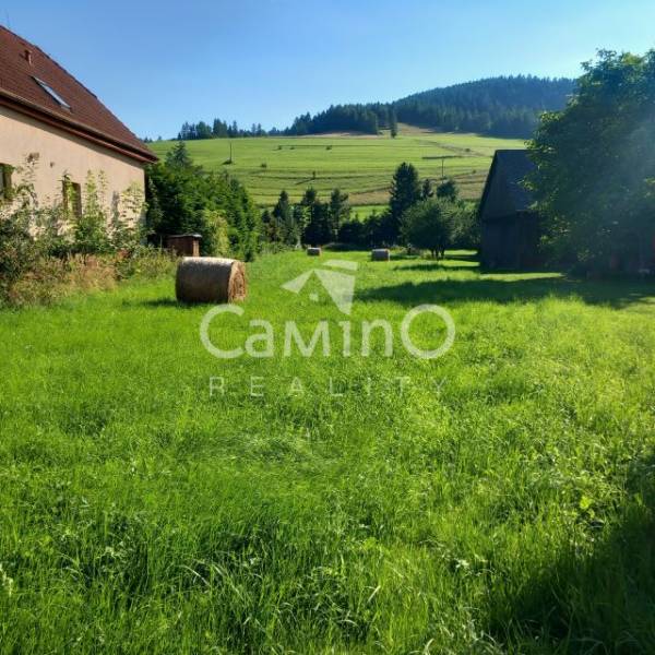 ZNÍŽENÁ CENA!!! Stavebný pozemok 1621 m2 v obci Reľov - Hagy. - Slnečná lúka s balíkmi sena pri dome, na pozadí sú svieže zelené kopce.