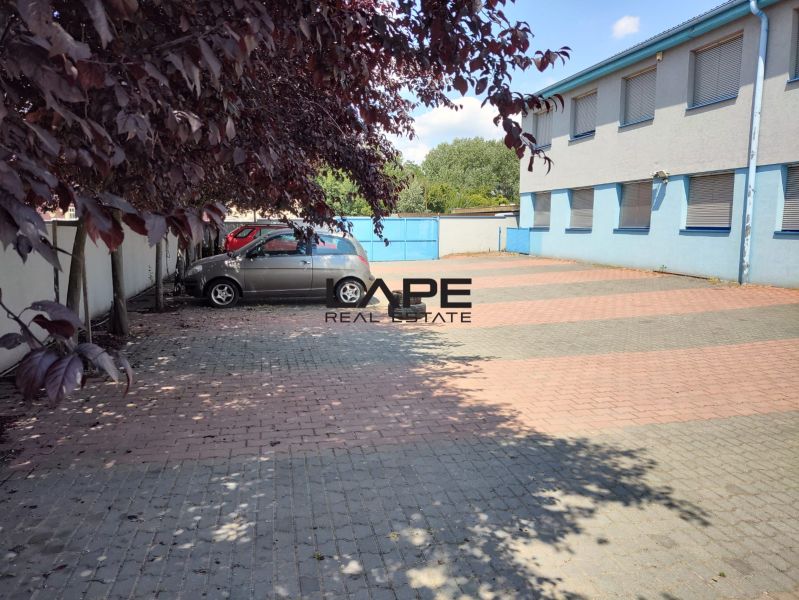 Prenájom - skladové priestory/kancelária, Vlčie hrdlo, Bratislava - Parkovisko pred modrou budovou, autá zaparkované na dlažbe, okolité stromy poskytujú tieň, kancelárie.