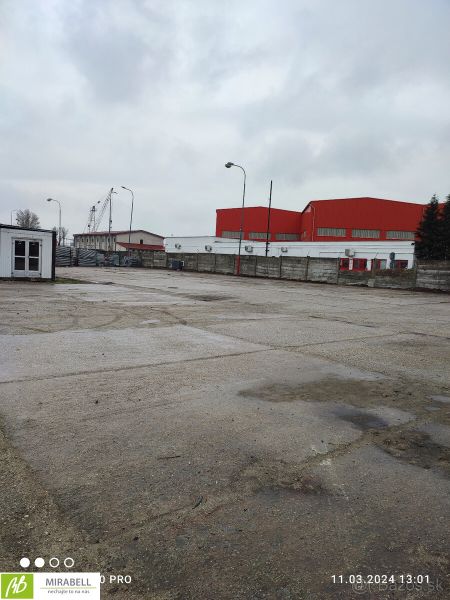 Spevnené plocha a lodné kontajnery v uzavretom areáli - Vajnory - Na ulici Pri starom letisku, pozemky - komerčné, prázdna plocha s budovami v pozadí.