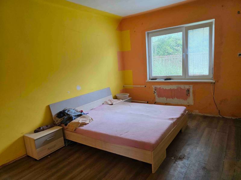 Dulovce - RODINNÝ DOM so 700 m2 POZEMKOM - Žltá izba rodinného domu s posteľou a nočným stolíkom, pripravená na renováciu.