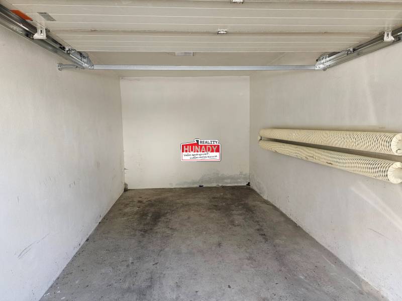 (16 m²) GARÁŽ NA PRENÁJOM V CENTRE - Interiér garáže s otvorenou bránou a vešiakmi na stene.