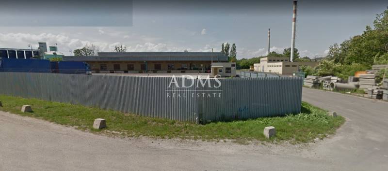 Skladový areál, Pribeník - Priestor s plechovým plotom a industriálnymi stavbami v Pribeníku, sklady a haly.