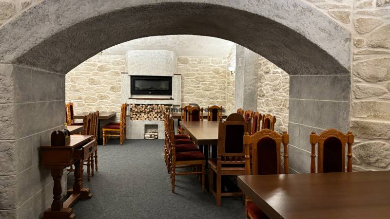 ODSTÚPENIE REŠTAURÁCIE v Nitre - Reštauračný interiér s kamennými stenami, drevenými stolmi, krbom a kreslami v gastro priestore.