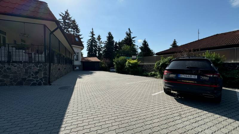 NA PREDAJ hotel s reštauráciou - Parkovisko pre hotely a penzióny s autom, stromami a budovou v pozadí.
