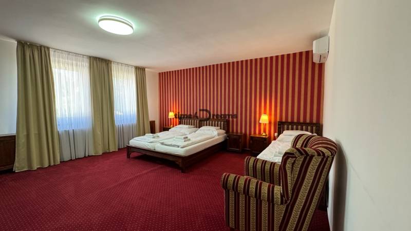 NA PREDAJ hotel s reštauráciou - Hotelová izba s červenými závesmi, dvojposteľou a kreslom. Hotely a penzióny.