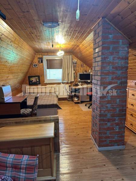Na predaj Rekreačný dom s rozľahlým pozemkom v Leviciach. - Podkrovná miestnosť v chate s dreveným interiérom a tehlovým pilierom.