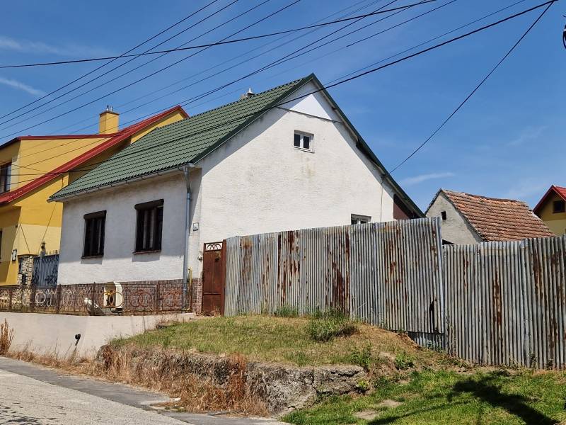 NA PREDAJ RODINNÝ DOM V OBCI ŠTEFANOV, OKRES SENICA - Rodinný dom v Štefanove s plechovým plotom a šikmou strechou pod modrou oblohou.