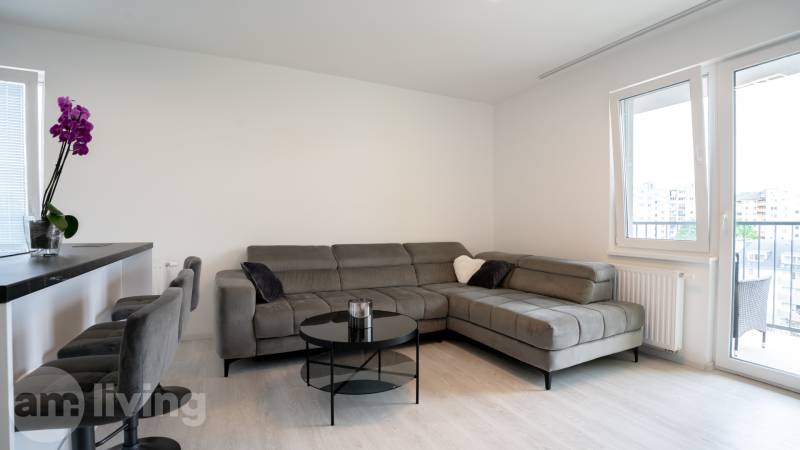 ZARIADENÝ - 3i v novostavbe 76 m2 + balkon - Trenčín - Obývacia izba v 3-izbovom byte s pohodlnou sivou sedacou súpravou a balkónom.