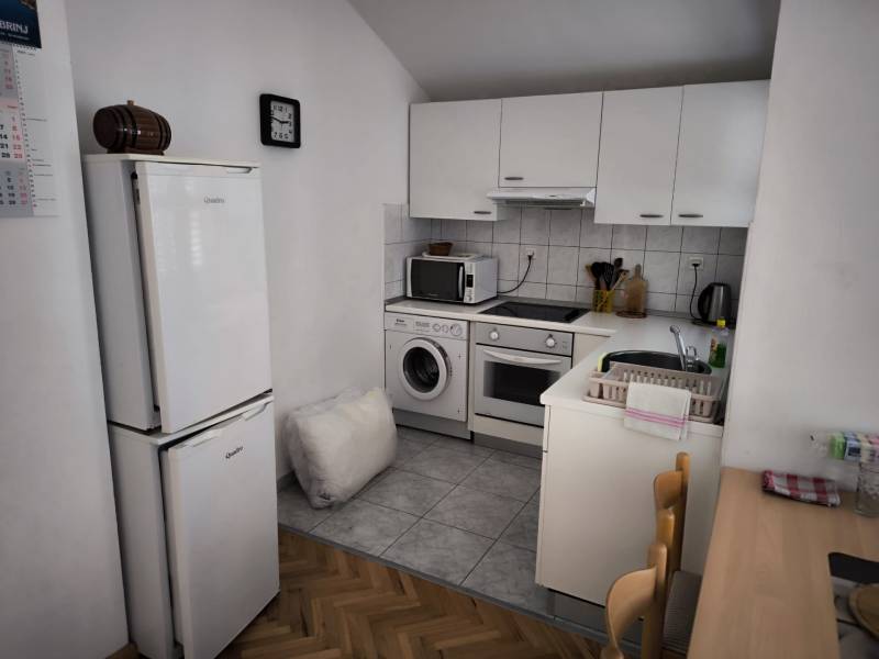 CHORVÁTSKO - Apartmány 1.rad od mora - SUKOŠAN, ZADAR - Kuchyňa v 1-izbovom byte s bielymi skrinkami, spotrebičmi a dreveným stolom.